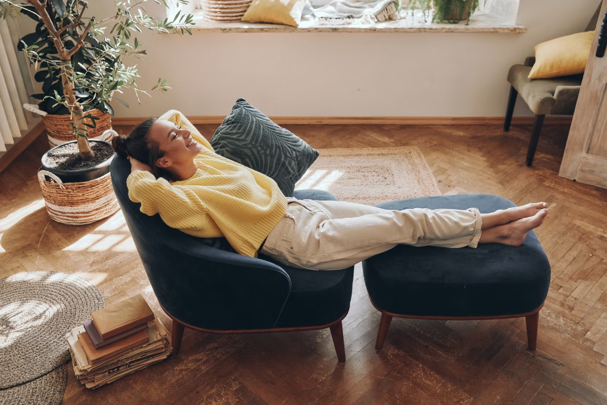 Mulher relaxando em poltrona com apoio para pernas e pés, em sua sala de estar.
